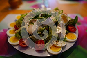 Closeup of delicious salad with boiled eggs, goat cheese and vegetables in a plate on the table