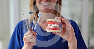 Closeup of dentist holding model of human jaw with teeth toothbrush mirror and dental instruments