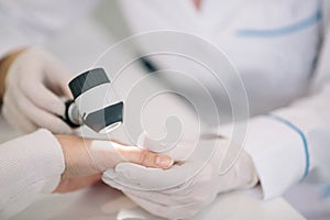 Closeup of dermatologist examining mole on hand of female patient in clinic