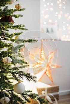 Closeup detail of christmas tree in stylish winter holiday interior with stars, lights, gifts and decoration