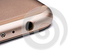 Closeup detail of 3.5mm audio jack connector hole on bottom of rose gold coloured mobile phone, isolated white background