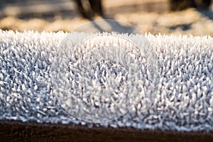 Closeup detail of white crystallized cold hoar frost covering a frozen handrail outside an early fresh winter morning