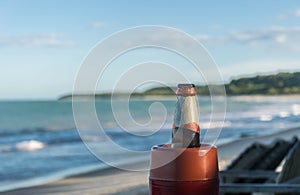 Closeup and detailed view of the upper part of a beer bottle with a red and white aluminium label, in front of a