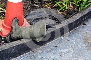 Closeup of a dirty black rubber boots on a road with a red traffic cone at the garden with tiled floor