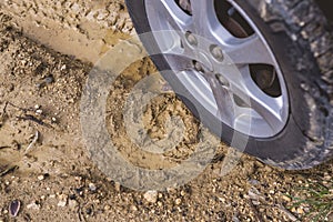 Closeup of a dirty tire driving through a muddy and unpaved rural road, leaving depressed tread marks. A damp path during the