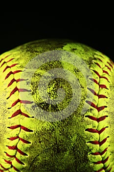 Closeup of a dirty, yellow softball with red seams.