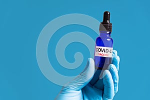 Closeup of doctor hand with gloves holding covid-19 vaccine blue vial on blue background. concept of science and coronavirus