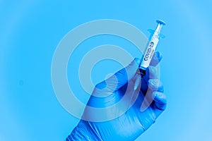 Closeup of doctor hand with gloves holding covid-19 vaccine syringe on blue background. concept of science and coronavirus vaccine