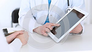 Closeup of a doctor and patient sitting at the desk. Physician pointing into tablet pc. Medicine and health ca