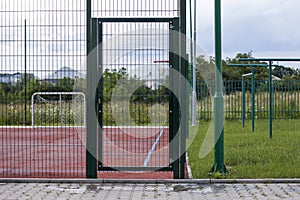 Closeup of door gate entrance to soccer or football field playground with bright red soft rubber flooring and protective net fence