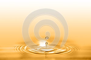 Closeup on drop of cosmetic golden oil liquid creating a circular wave.