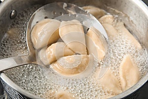 Closeup of dumplings on skimmer over stewpan with boiling water.