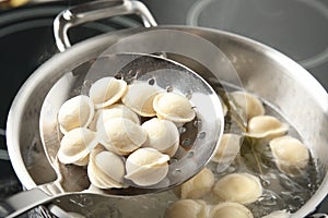 Closeup of dumplings on skimmer over stewpan with boiling water
