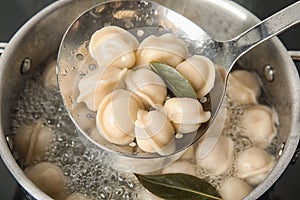 Closeup of dumplings on skimmer over stewpan with boiling water