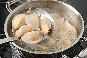 Closeup of dumplings on skimmer over stewpan with boiling water.