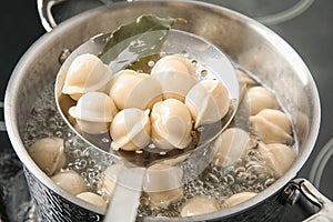 Closeup of dumplings on skimmer over stewpan with boiling water