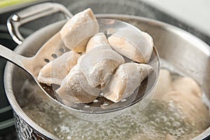 Closeup of dumplings on skimmer over stewpan with boiling water