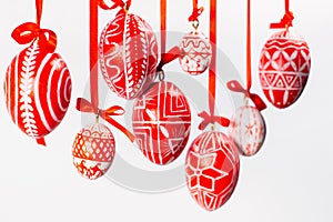 Closeup Easter eggs with folk Ukrainian pattern hang on red ribbons with bows on white background. Ukrainian traditional eggs