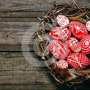 Closeup Easter red eggs with folk white pattern inside bird nest on rustic wood board. Top view