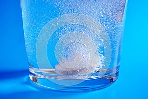 Closeup of effervescent tablet dissolving in glass of water on blue background