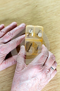 Closeup of an elderly senior woman& x27;s hands taking her medication for the week in a pill box on wooden table, business