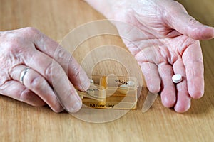 Closeup of an elderly senior woman& x27;s hands taking her medication for the week in a pill box on wooden table, business,health