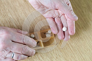 Closeup of an elderly senior woman& x27;s hands taking her medication for the week in a pill box on wooden table, business,health