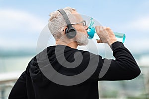 Closeup of elderly sportsman drinking water during workout outdoors