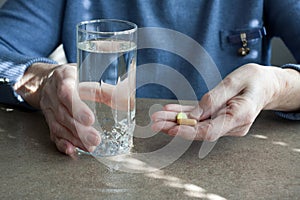 Closeup of elderly woman hand holding pills and glass of drinking water. Senior woman is going to take medicines for illnesses.