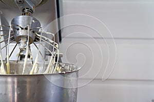 Closeup of electric mixer with whipped smooth dough for cake. Batter being whipped. Mixing white dough in bowl with motor mixer