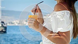 Closeup of elegant brunette woman enjoying her cocktail while relaxing at beach and looking on the yachts and ocean