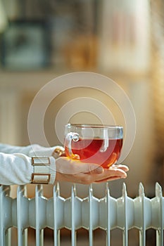 Closeup on elegant woman near radiator and holding tea cup