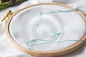 Closeup of an embroidery process, a green thread in a needle. Wooden embroidery frame for needlework. Workplace for