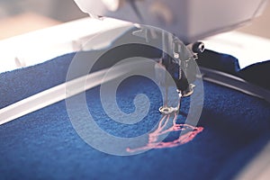 Closeup on embroidery progress of pink magnolia on boiled wool in trendy classic blue color in moody light