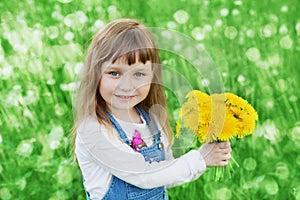 Closeup emotional portrait of cute little girl with dandelion flowers bouquet standing on a green meadow