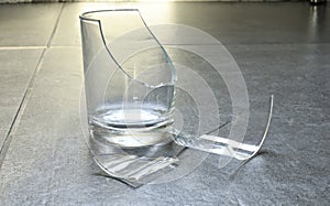 Closeup of empty cracked drinking glass isolated on grey tile background, beverage glass cruash small shattered piece. Accident in