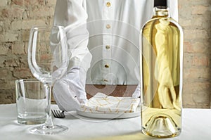 Closeup of empty wine glass and bottle of white wine, waiter servig the table