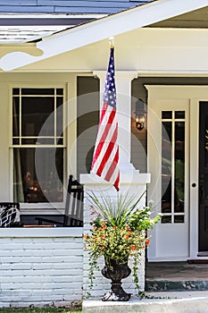 Closeup of entrance to cottage house with beautiful flowers in a pot and American flag by porch
