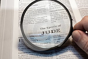 closeup of The epistle of Jude from Bible using a magnifying glass to enlarge print.