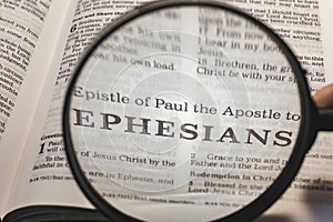 closeup of the epistle of Paul to the Ephesians from Bible using a magnifying glass to enlarge print.