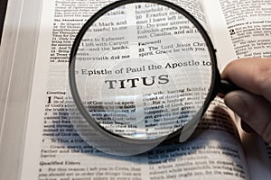 closeup of the epistle of Titus from Bible using a magnifying glass to enlarge print.