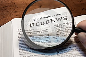 closeup of The epistle to the Hebrews from Bible using a magnifying glass to enlarge print.