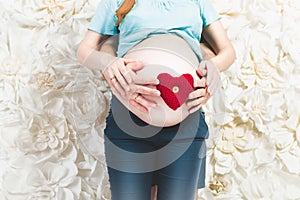 Closeup of expectant parents holding red hearth on stomach