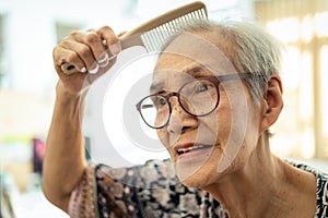 Closeup of face of beautiful old people brushing hair with comb in her hand,happy asian senior woman enjoy combing hair,clean