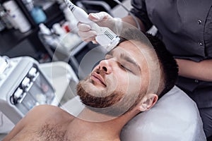 Closeup of face of beautiful relaxing man undergoing hardware cosmetology procedure in spa