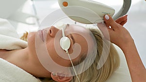 Closeup face of blonde female wearing protective glasses getting photo rejuvenation procedure in beauty salon