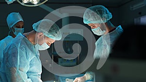 Closeup face of concentrated surgeon male with his assistants sutures stomach skin during surgery with neat stitches