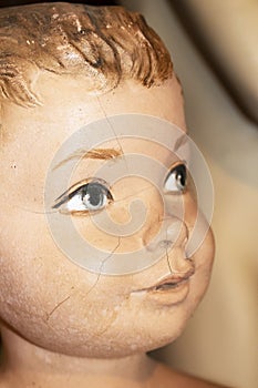 Closeup of face of cracked vintage little boy mannequin with foreground painted eye in focus