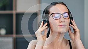 Closeup face young Asian woman listening music in headphones with closed eyes relaxing at home