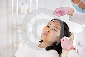 Face of young female client receiving injections during lip enhancement procedure, professional cosmetologist hands in photo